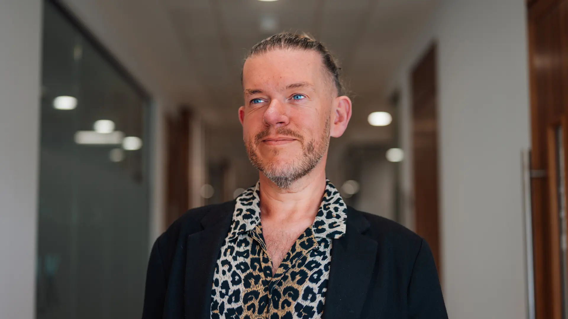 Man with slicked back hair, leopard shirt and blazer gazing off into the distance