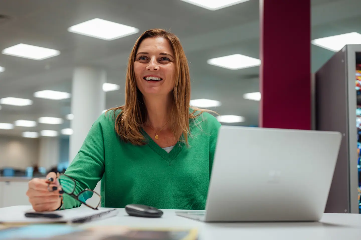 Woman in a green shirt on a laptop in an office environment, smiling