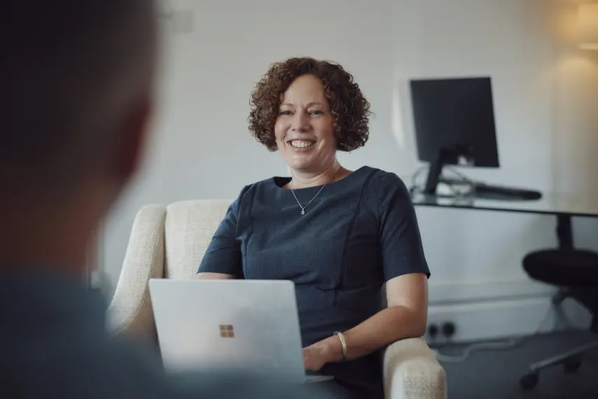 Female Travel Counsellor with laptop on knee and computer monitor in the background