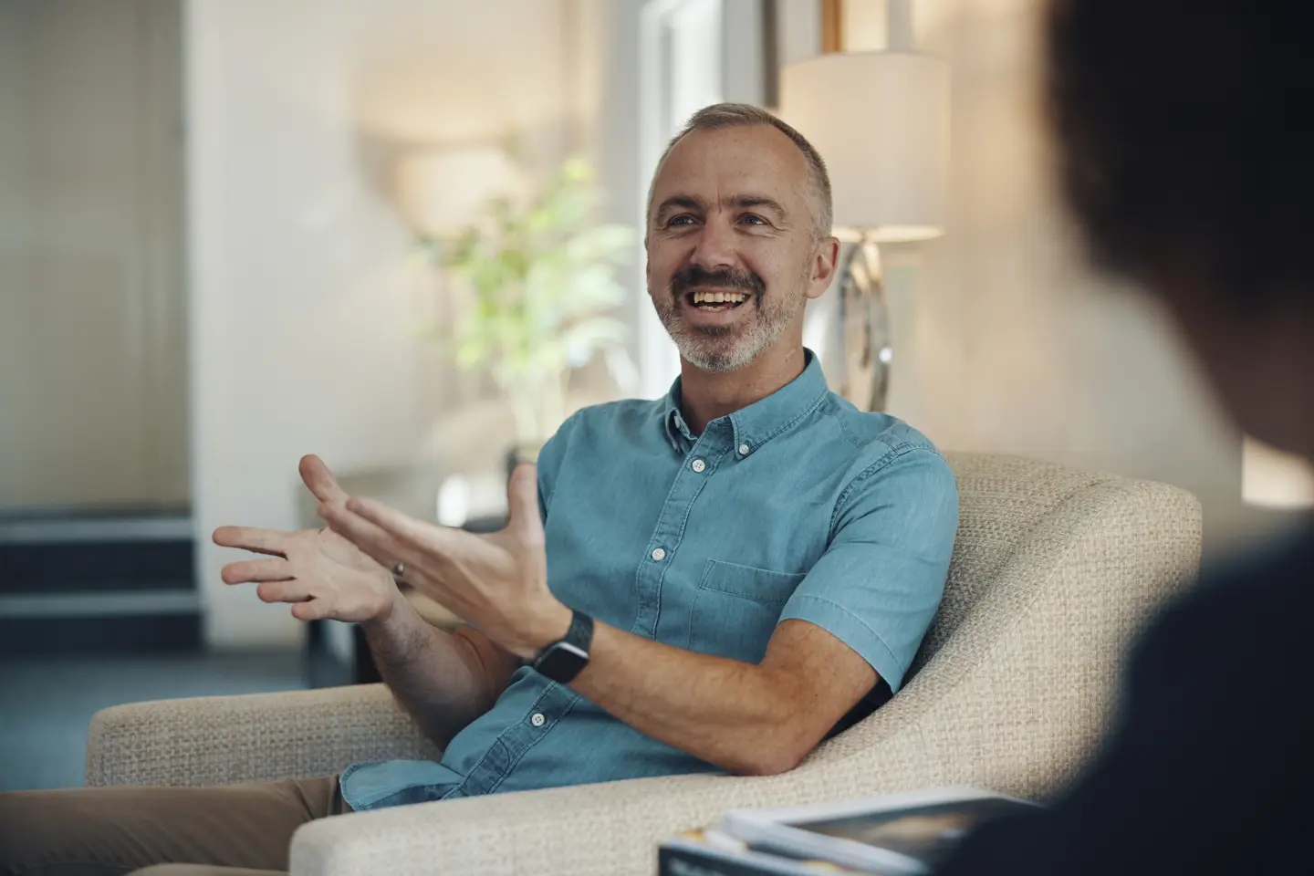 Male Travel Counsellor sat in a chair, smiling and gesturing with his hands